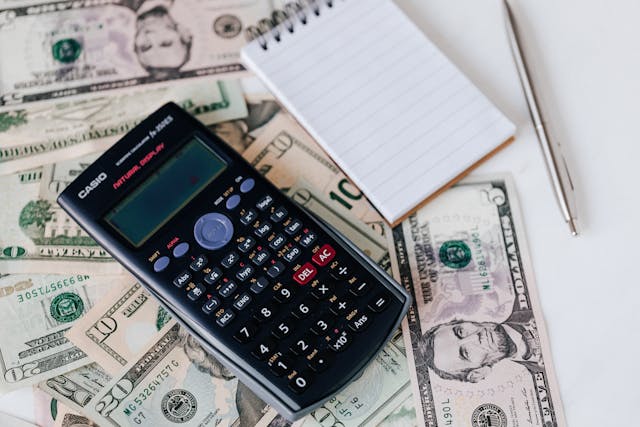 A calculator and a notebook resting on top of some American dollar bills.