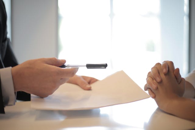 A person passing a contract and a pen over a table to another person.